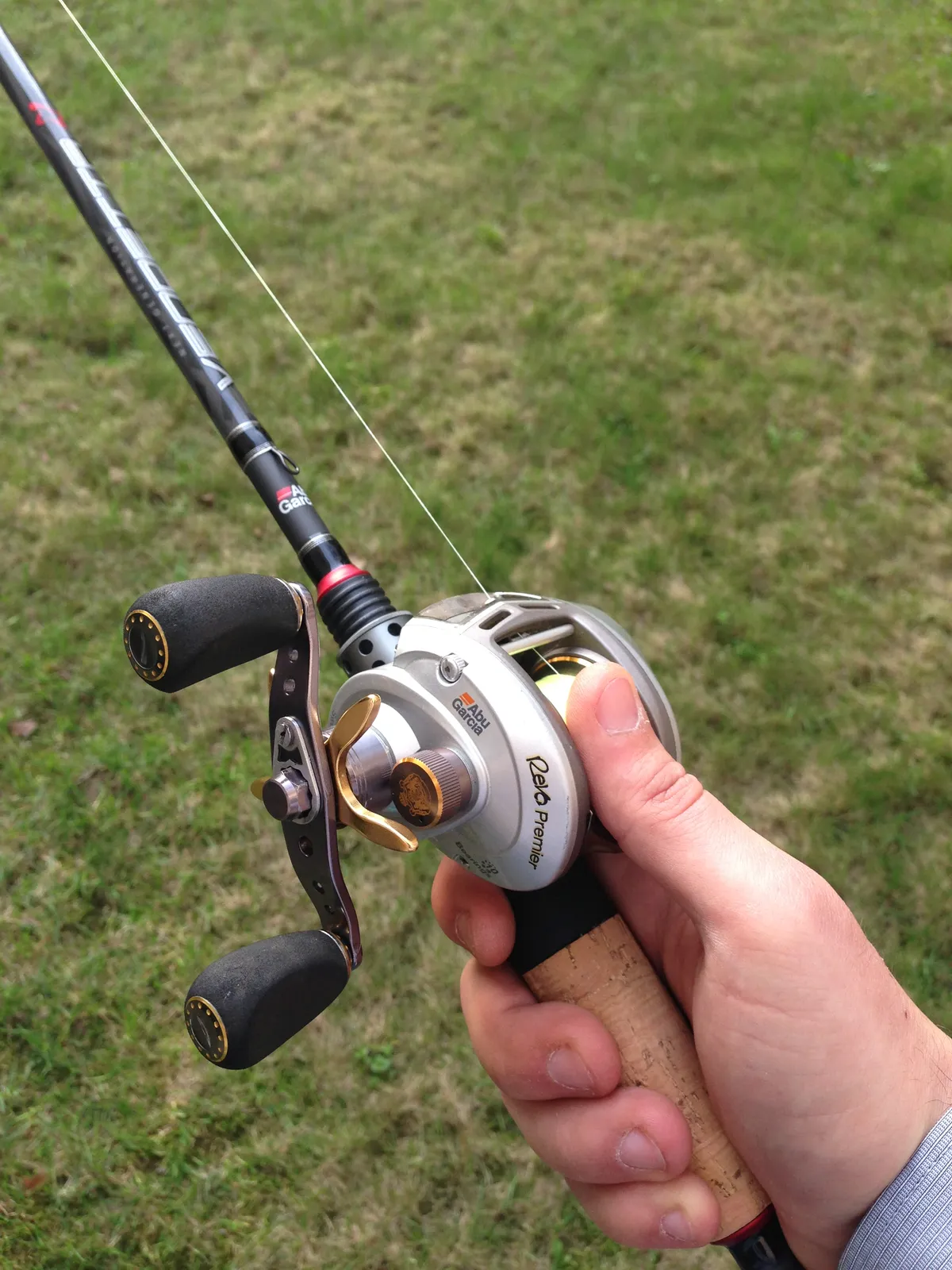 A low-profile baitcasting reel held on a rod, with a thumb beside its exposed spool and the handle to the left.