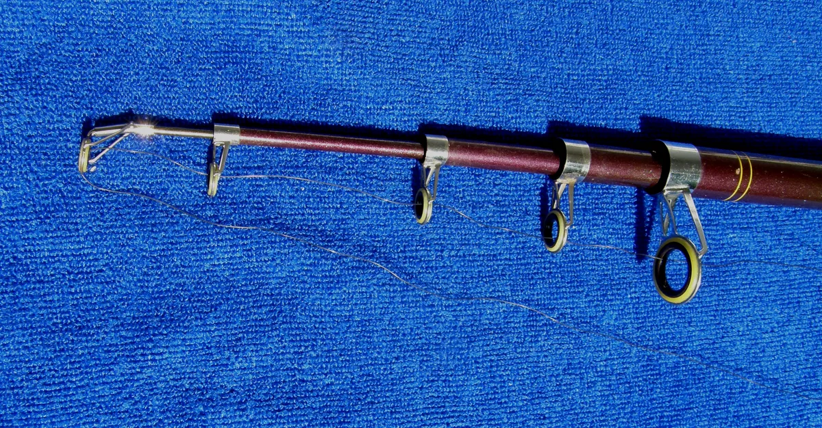 The tip section of a telescopic rod lying on a blue towel, with line threaded through four ring guides that get smaller toward the tip and through the tip top at the end.