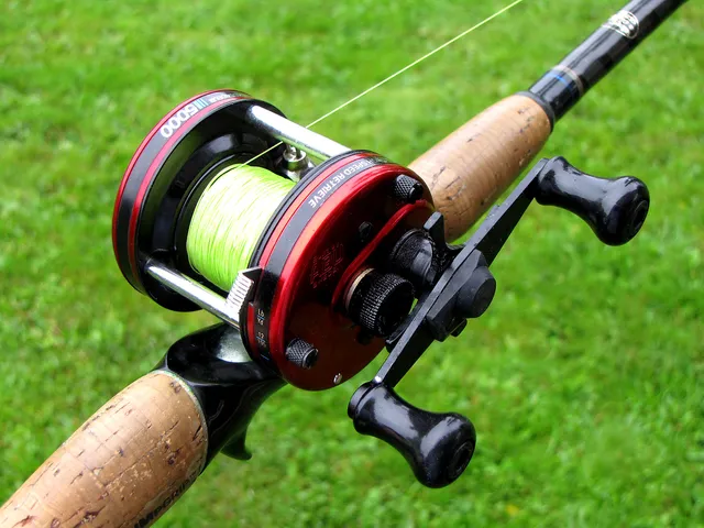 A red round-profile baitcasting reel with an exposed line-filled spool and twin handle, mounted on a cork-handled rod.