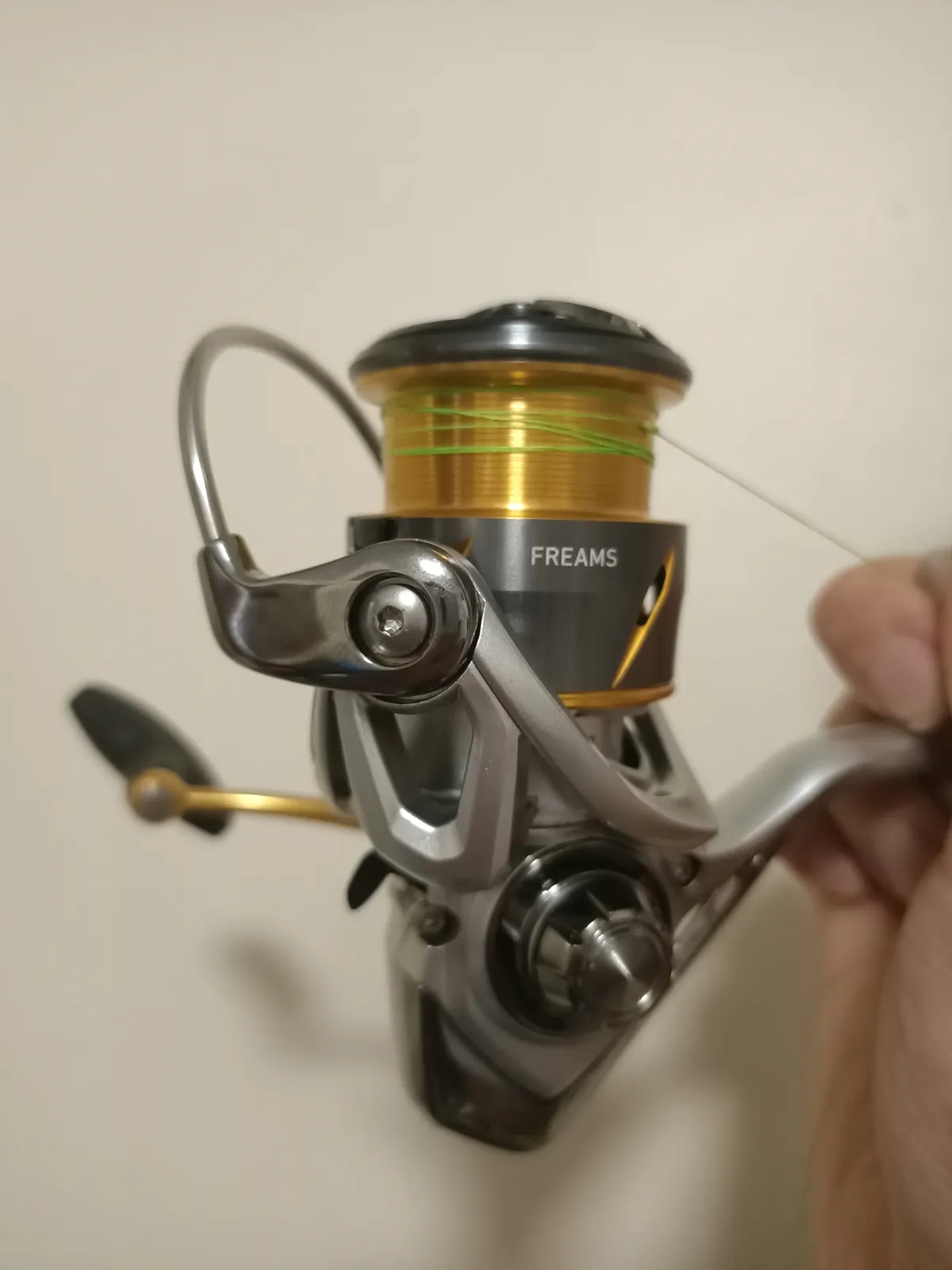 A spinning reel held by its stem with the bail wire flipped open above the spool, a few turns of line on the spool and the line roller on the rotor arm in front.