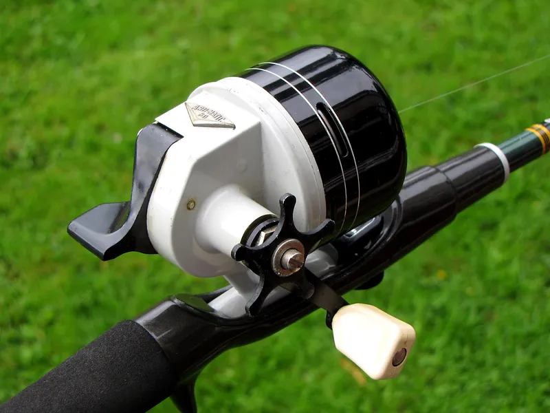 A vintage closed-face spincast reel mounted on a rod, with its enclosed front, rear release lever and handle visible.
